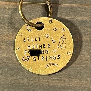 以下が含まれることがあります： キーリングが付いた金色の金属タグ。タグには「Billy Mother F***ing Strings」という文字と星とロケットのデザインが書かれています。