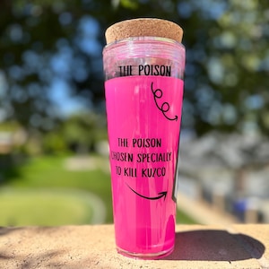 May include: A clear tumbler with a pink interior and a cork lid. The text "THE POISON" is printed at the top, with "THE POISON CHOSEN SPECIALLY TO KILL KUZCO" below. Black arrows and swirls decorate the design.
