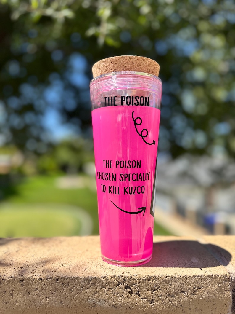 May include: A clear tumbler with a pink interior and a cork lid. The text "THE POISON" is printed at the top, with "THE POISON CHOSEN SPECIALLY TO KILL KUZCO" below. Black arrows and swirls decorate the design.