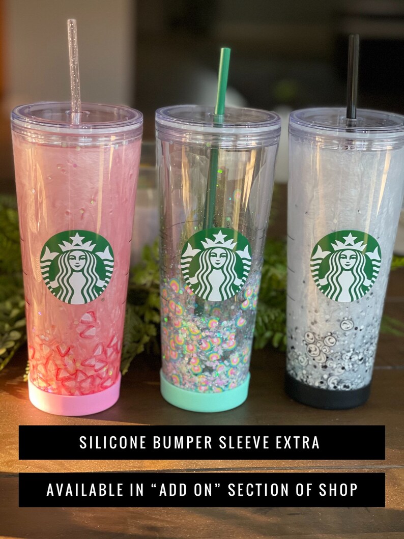 May include: Three clear plastic tumblers with silicone sleeves. The tumblers have a Starbucks logo and are filled with glitter. The sleeves are pink, teal, and black.