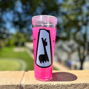 May include: A clear, pink tumbler with a black and white llama graphic. The tumbler has a clear lid and is filled with a pink liquid. The graphic is inside a white and black border with arrows pointing towards the llama.
