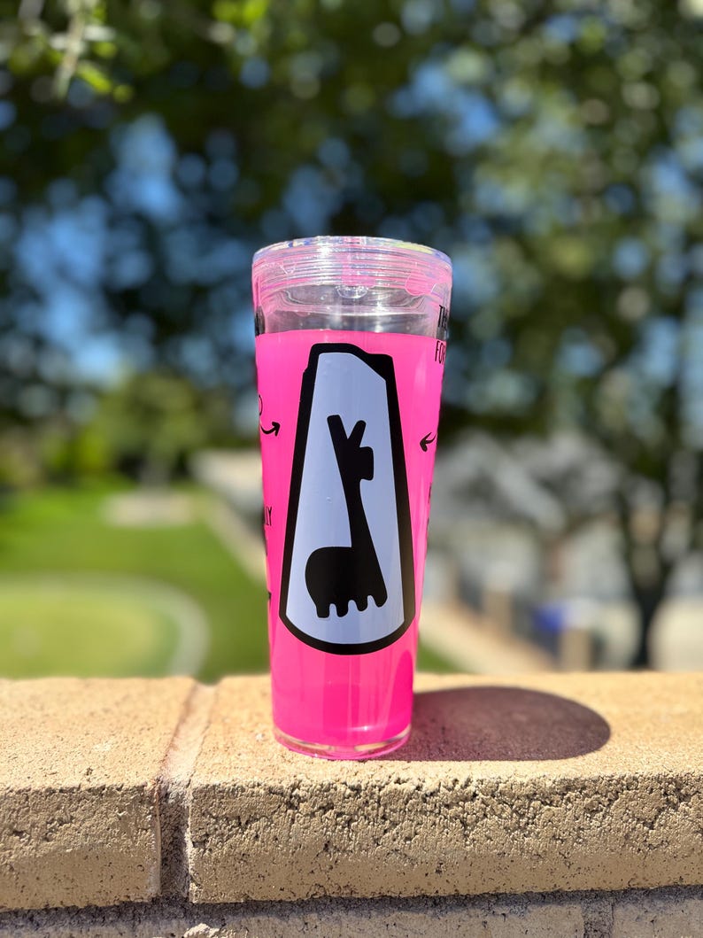 May include: A clear, pink tumbler with a black and white llama graphic. The tumbler has a clear lid and is filled with a pink liquid. The graphic is inside a white and black border with arrows pointing towards the llama.