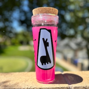 May include: A tall, clear tumbler with a bright pink exterior and a cork lid. The tumbler features a white graphic of a llama inside a black outline. The text "FO" is visible on the side of the tumbler.