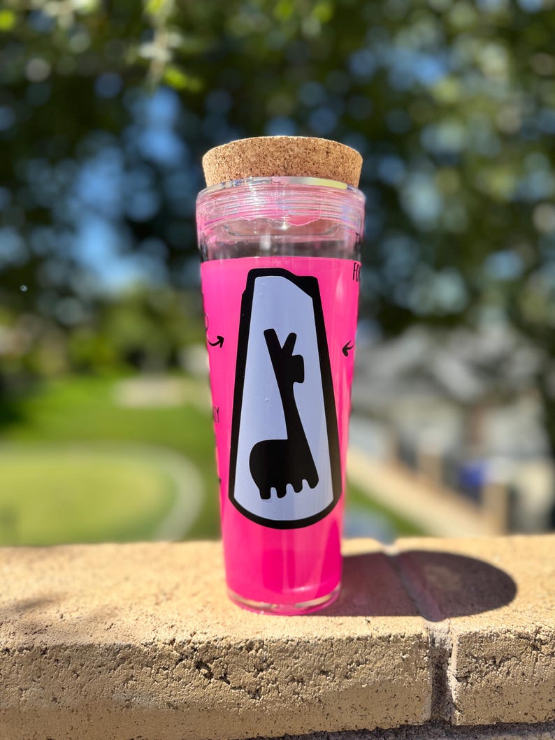 May include: A tall, clear tumbler with a bright pink exterior and a cork lid. The tumbler features a white graphic of a llama inside a black outline. The text "FO" is visible on the side of the tumbler.