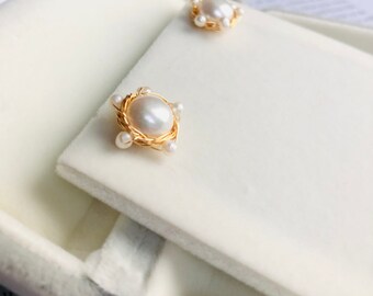 May include: A pair of pearl earrings with a gold wire design. The pearls are white and the wire is a shiny gold color. The earrings are displayed in a white velvet box.