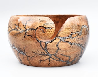 Könnte beinhalten: Holz-Garn-Schale mit einem einzigartigen, natürlichen Holzmaserungsmuster mit einem wirbelnden, hellfarbigen Design. Die Schale hat eine geschnitzte Öffnung, durch die das Garn geführt werden kann.