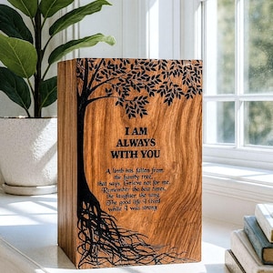 May include: A wooden box with a tree design and the words "I AM ALWAYS WITH YOU" engraved on the front. The box has a natural wood grain finish and includes a poem. The box is sitting on a white surface.
