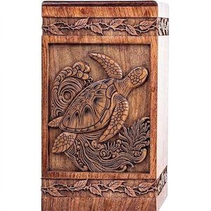 May include: Wooden box with a carved sea turtle design. The box is rectangular with a dark brown top and bottom, and a lighter brown body. The sea turtle is carved in detail, with waves and foliage surrounding it.