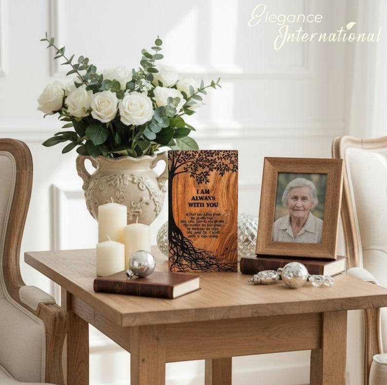 May include: A wooden plaque with the text "I AM ALWAYS WITH YOU" and a tree design, a framed photo, and a vase of white roses sit on a wooden table. The scene includes candles, books, and decorative silver spheres.