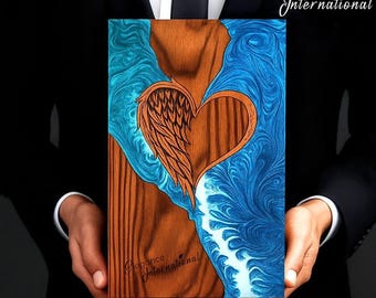 May include: A wooden art piece featuring a heart and wing design. The heart and wing are carved from wood, with a blue and white resin background. The piece is held by a person wearing a black suit. The text "Elegance International" is visible.