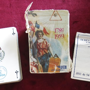 May include: A deck of playing cards with a white card showing the number 1 and a clover symbol. The card deck is next to a card box with the text "1789 1989" and a booklet that says "54 REVOLUTION 1789-1989".