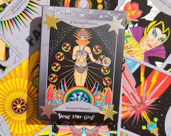 May include: A deck of tarot cards featuring a central card titled 2 The High Priestess, Shroud of Mystery, and Your Star Girl. The card displays a figure in a headdress surrounded by colorful orbs, a rainbow, and stars on a black background.