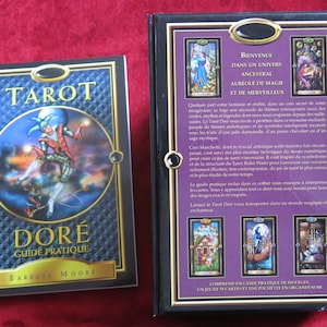 May include: Tarot Dore deck with a guidebook. The box features a black background with gold accents and images of the cards. The guidebook has a black and gold cover with the title "Tarot Dore Guide Pratique" and the author's name "Barbara Moore".