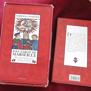 Op de afbeelding: Een rode doos en boekenset met "DAS TAROT DE MARSEILLE" van Corinna Harder. De doos heeft illustraties van figuren en engelen, met tekst in het Duits. De achterkant van het boek heeft tekst en een bloemenontwerp.