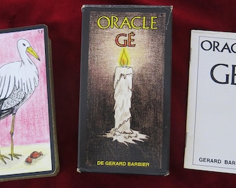 May include: A deck of Oracle Gé cards featuring a stork illustration, a black box with a lit candle graphic labeled ORACLE GÉ DE GERARD BARBIER, and a white instruction booklet with the text ORACLE GÉ GERARD BARBIER printed in black ink.