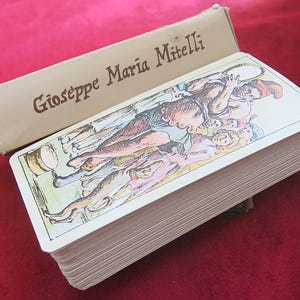Puede incluir: Una baraja de cartas con una ilustración colorida de un grupo de personas en el frente. La caja está etiquetada "Giuseppe Maria Mittelli".