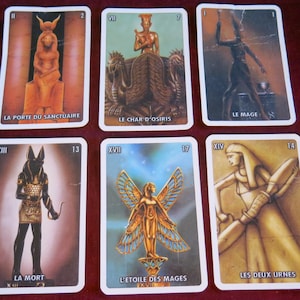 Puede incluir: Cartas de tarot con temas egipcios. Las cartas presentan ilustraciones de una mujer en una puerta, un carro, un mago, una figura esquelética, una figura alada y una mujer con dos urnas. Las cartas están numeradas 2, 7, 1, 13, 17 y 14.