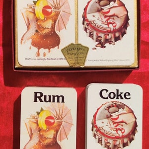 May include: Two playing cards featuring illustrations of a rum and coke drink. The rum card depicts a glass with a cherry, lemon wedge, and a pink umbrella. The coke card shows a Coca-Cola bottle cap with a red and white logo. The cards are from Waddingtons Playing Cards.