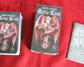 Könnte beinhalten: Ein Gothic Tarot Deck mit einem roten Drachen auf dem Cover. Die Schachtel ist schwarz mit goldenen Akzenten. Das Deck enthält ein Handbuch mit Anweisungen in Englisch, Französisch, Spanisch und Portugiesisch.