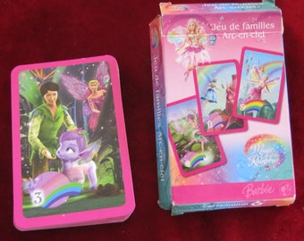 May include: A pink deck of playing cards featuring a Barbie Magic of the Rainbow design. The front of the card shows a fairy, a boy, and a unicorn-like creature in a forest setting. The back of the card shows a rainbow and the text "Barbie Magic of the Rainbow".