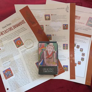May include: A deck of Oracolo Tibetano cards in a black box featuring a colourful illustration of a figure, placed over several informational sheets with Spanish text, including the title El Vehículo del Diamante and various diagrams.