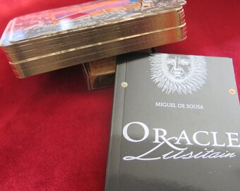 Puede incluir: Una baraja de oráculo negra y dorada con un diseño de sol y rostro en la parte delantera. El texto en la parte delantera dice "Oracle Lusitan" y "Miguel de Sousa".