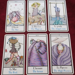 May include: A set of tarot cards with detailed illustrations and text. The cards depict figures like "The Star," "The Magician," and "The Hanged Man." Each card has a white border and includes both French and English text.