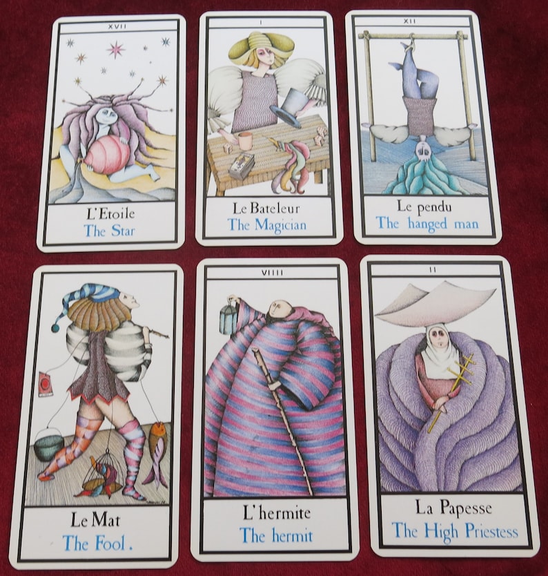 May include: A set of tarot cards with detailed illustrations and text. The cards depict figures like "The Star," "The Magician," and "The Hanged Man." Each card has a white border and includes both French and English text.