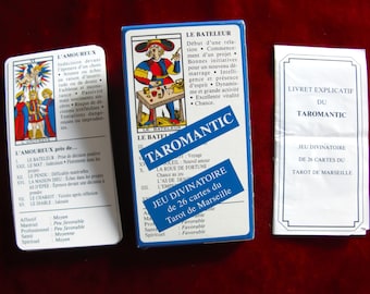 Op de afbeelding: Een blauwe en witte doos met Tarotkaarten met de titel "Taromantic Jeu Divinatoire de 26 cartes du Tarot de Marseille". De doos toont een afbeelding van een man die een toverstaf vasthoudt en een kleine tafel met een beker, een munt en een zwaard erop. De doos bevat ook een klein boekje met de titel "Livret Explicatif du Taromantic".