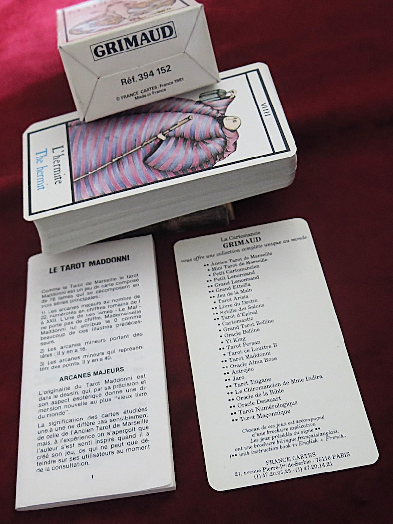 May include: A tarot card deck with a box, branded "GRIMAUD". The cards display an illustration of a robed figure. The box has the text "R&eacute;f. 394 152". Includes instruction booklets. The cards and box are made in France.