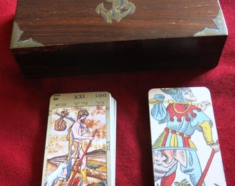 May include: A wooden box with brass accents and an anchor design on the lid. The box contains a deck of tarot cards with a card showing a man with a bag and a dog, and another card showing a jester.