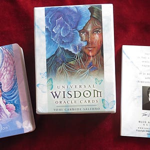 May include: A set of Universal Wisdom Oracle Cards, featuring a box with a woman's face and blue flower art. The deck includes a card with an angel illustration and the word "Intention."