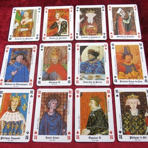 K&ouml;nnte beinhalten: Ein Satz von 12 Spielkarten mit Portr&auml;ts historischer Pers&ouml;nlichkeiten. Jede Karte hat oben links ein schwarzes Pik-Symbol und unten rechts ein rotes Herz-Symbol. Die Karten sind wei&szlig; mit schwarzem Rand und zeigen farbenfrohe Illustrationen historischer Pers&ouml;nlichkeiten.