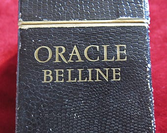 Può includere: Una scatola nera, strutturata con scritte dorate che recitano "ORACLE BELLINE". La scatola ha una forma rettangolare e sembra essere fatta di pelle o materiale simile. I bordi della scatola sono leggermente usurati.