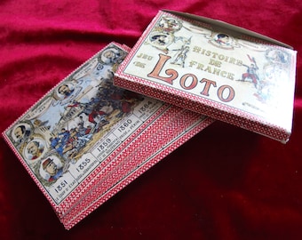 Peut inclure: Deux boîtes de jeu vintage pour un jeu de loto sur le thème de l'histoire de France. La boîte du dessus est blanche avec des accents rouges et noirs et porte l'inscription "Jeu de L'oto Histoire de France". La boîte du dessous est rouge et blanche avec un motif de petits carrés rouges et présente une chronologie de l'histoire de France de 1851 à 1864.