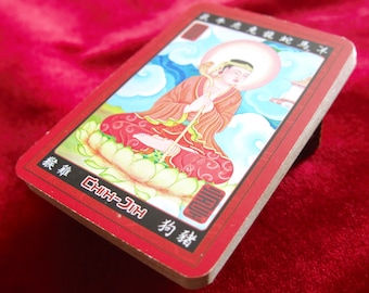 Puede incluir: Una tarjeta roja con una ilustración colorida de una persona sentada en una flor de loto. La tarjeta tiene texto chino que dice "Chih-Ji" y "Dog Deity".