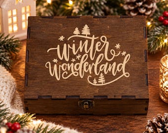 May include: A rectangular dark brown wooden box with a hinged lid featuring the laser-engraved text "winter wonderland" in a cursive script, accented by small pine tree and snowflake icons, and a metal latch on the front edge.