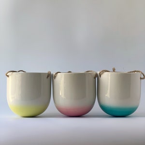 May include: Three ceramic hanging planters with a white glaze and a colored gradient at the bottom. The planters are yellow, pink, and blue.