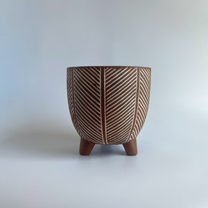May include: A brown ceramic planter with a white chevron pattern and three legs.
