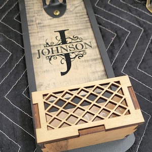Puede incluir: Abrebotellas de madera con marco de metal negro y una pequeña caja de madera con diseño de celosía. El abrebotellas tiene una inscripción personalizada que dice "J JOHNSON".