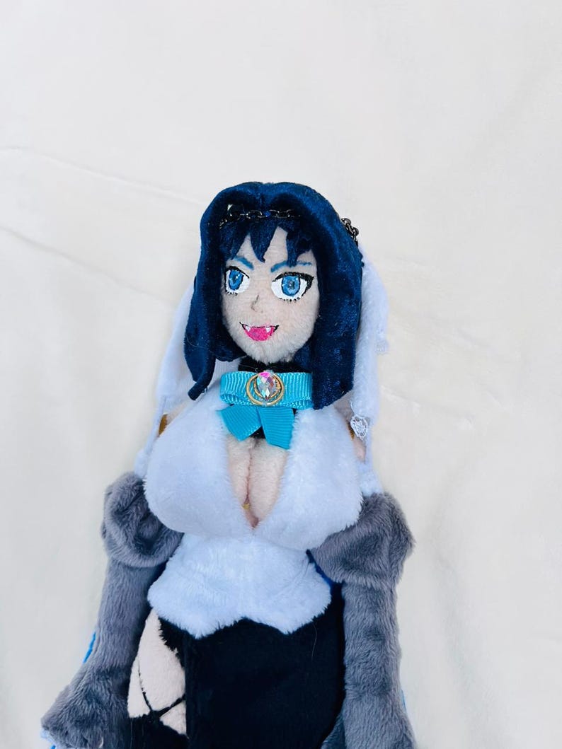 May include: A plush toy of a female anime character with long black hair, wearing a blue and white dress with a blue bow and a jeweled collar. The toy has a white background.