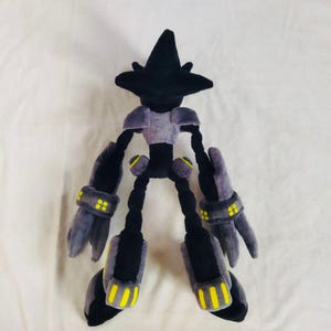 May include: A plush toy robot character with a black head and limbs, a grey torso, and grey arms and legs with yellow detailing. The toy is made of soft fabric and is designed to resemble a video game character. The toy is on a white background.