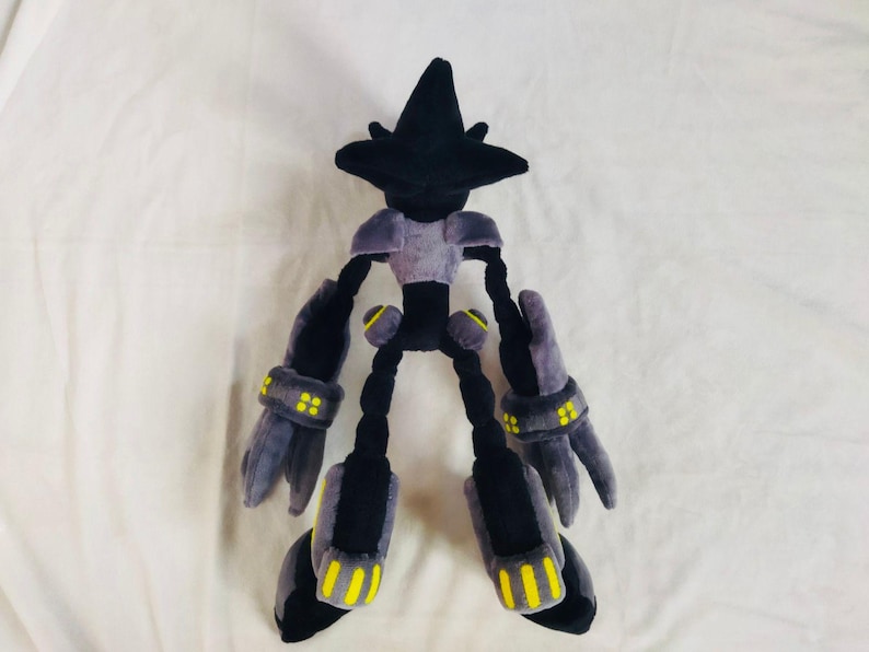 May include: A plush toy robot character with a black head and limbs, a grey torso, and grey arms and legs with yellow detailing. The toy is made of soft fabric and is designed to resemble a video game character. The toy is on a white background.