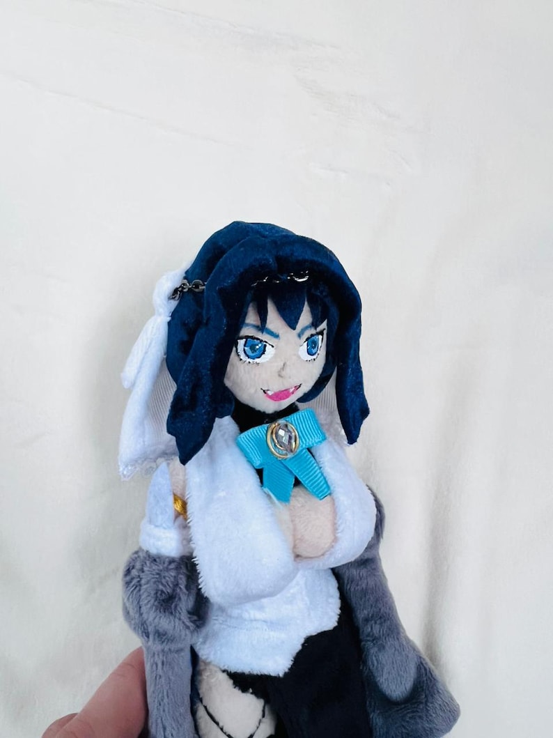 May include: A plush toy with blue hair, a blue hooded cloak, a white shirt, a blue bow, and a gray coat.