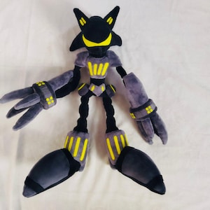 May include: A plush toy robot character in black, grey, and yellow. The toy has a distinctive head shape, large hands, and feet. The robot's body features yellow accents and is posed on a white surface.