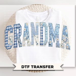 May include: White t-shirt with the word "GRANDMA" in blue patchwork letters. The letters feature various blue patterns, including gingham and floral prints. The text "DTF TRANSFER" is displayed on a banner below the shirt.