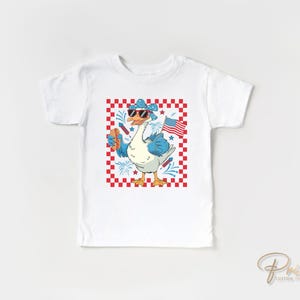 May include: White t-shirt with a graphic of a goose wearing sunglasses and a bandana, holding a hot dog and a small American flag. The goose is standing on a red and white checkered background.