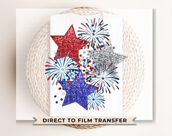 May include: White t-shirt featuring a patriotic design with red, silver, and blue glitter stars and fireworks. The design includes the text "DIRECT TO FILM TRANSFER" at the bottom, suitable for Independence Day celebrations.