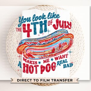 Op de afbeelding: Wit T-shirt met een kleurrijke afbeelding van een hotdog en de tekst "You look like the 4th of July makes me want a hot dog real bad." Het ontwerp gebruikt rode, blauwe en oranje kleuren, perfect voor 4 juli vieringen.