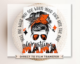 May include: A black and orange graphic design with a woman's face and hair in a bun. The text reads "Tell me what you see when your face hits the mat Wrestling Mama" and "Direct to Film Transfer".